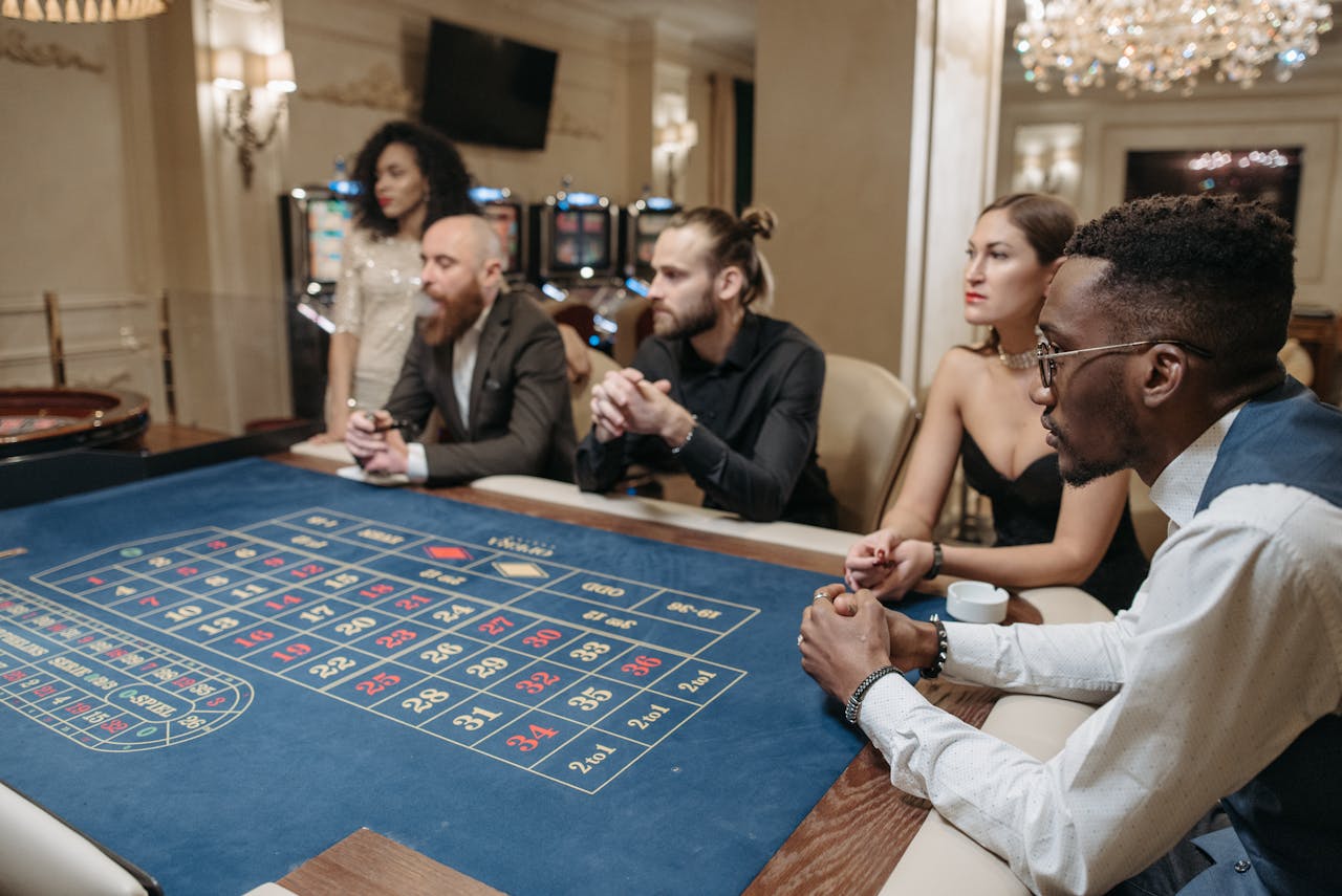 A diverse group of adults engaged in a roulette game at a luxurious indoor casino setting.