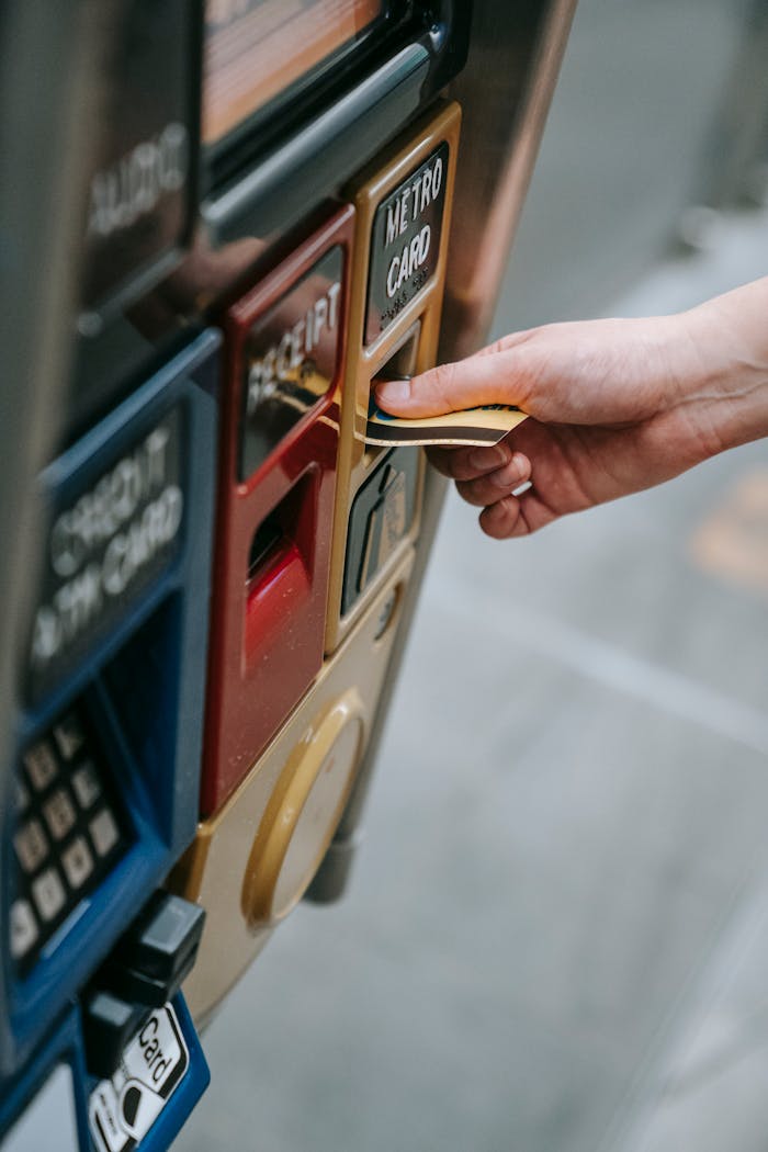 Close-up of a hand inserting a metro card into a ticket vending machine in an urban setting.
